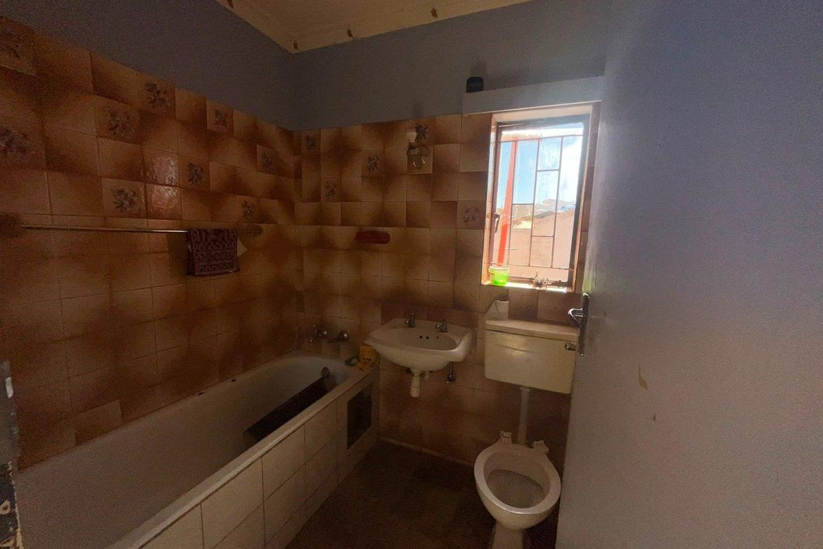 A dated bathroom featuring a bathtub, wall-mounted basin, and toilet with original tiled walls and a window with security bars.