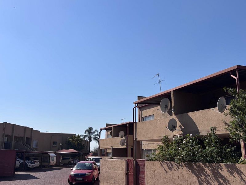Exterior view of an apartment complex featuring a paved driveway, carports, and multi-level units with balconies and satellite dish installations.
