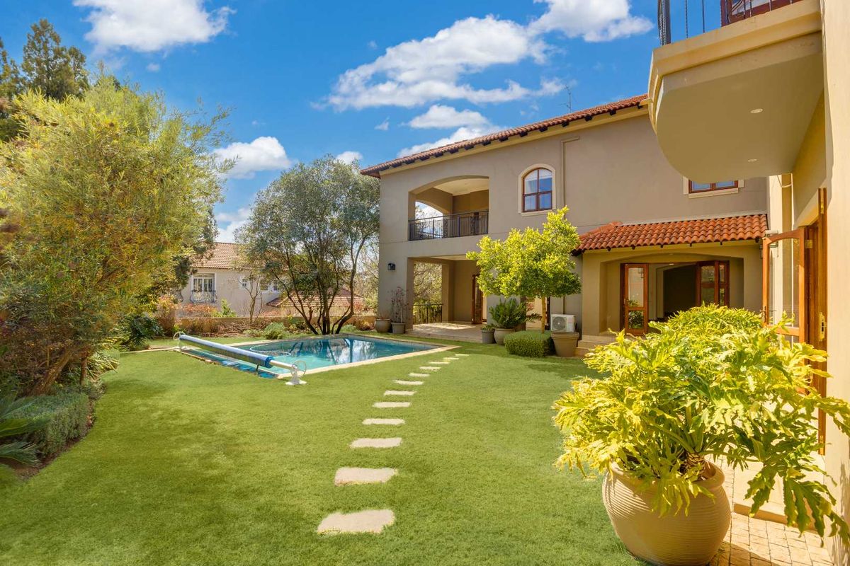 A well-maintained rear garden featuring a swimming pool, stone pathway, and a covered patio area attached to the double-story residence.