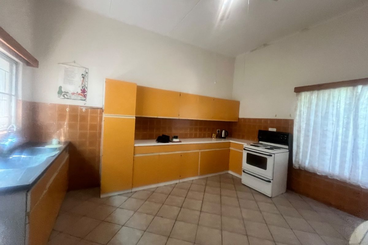 A dated kitchen featuring original yellow cabinetry, tiled backsplash, tiled flooring, and a freestanding stove, offering significant potential for a modern renovation.