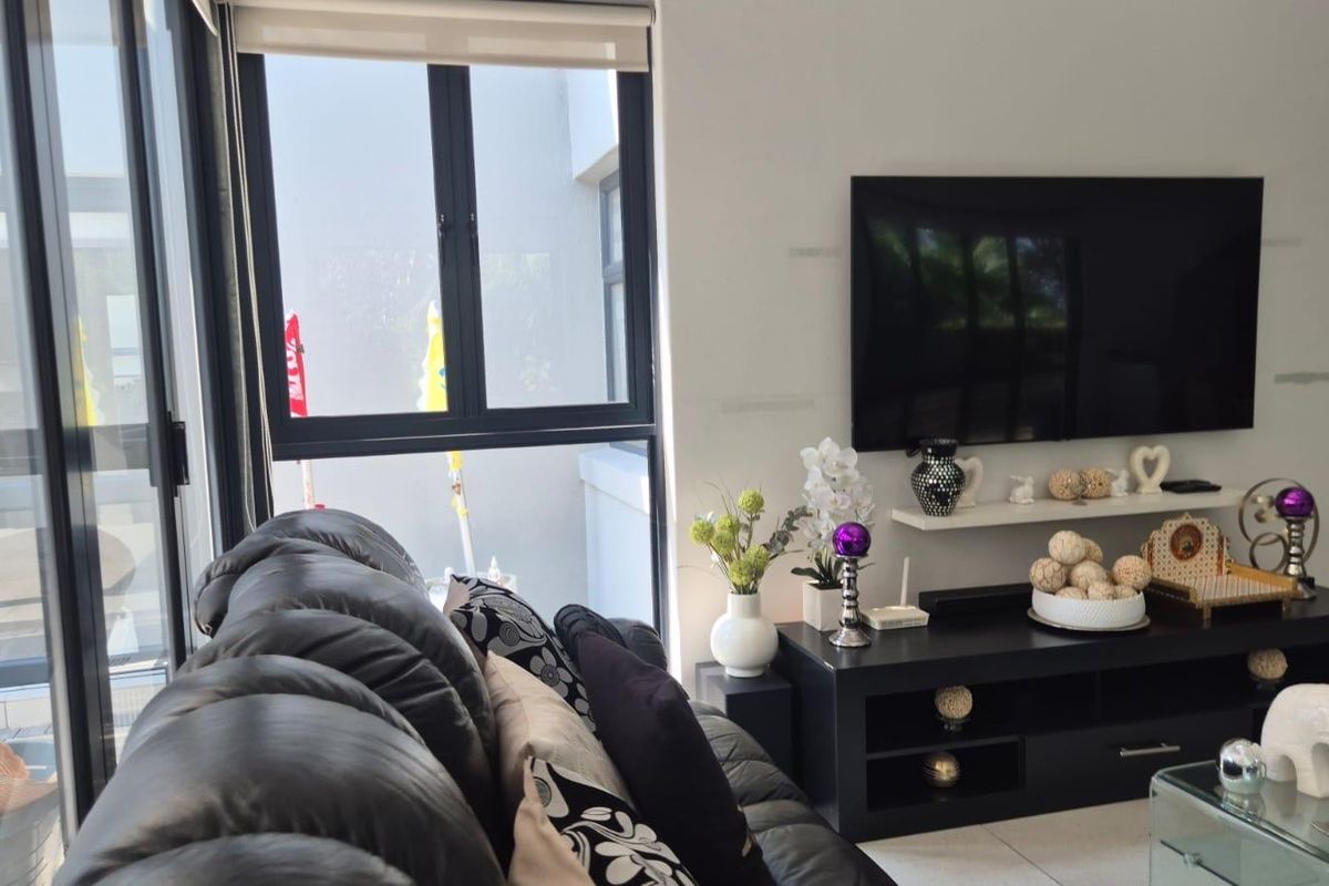 A bright living room featuring large sliding glass doors with black aluminium frames, roller blinds, and neutral tiled flooring.