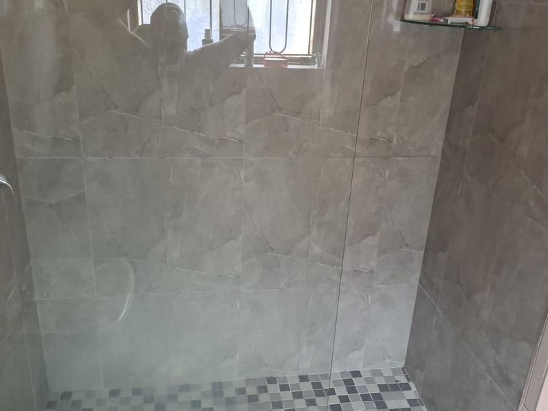A modern walk-in shower featuring grey marble-effect wall tiles, mosaic floor tiling, a glass screen, and a chrome shower mixer.