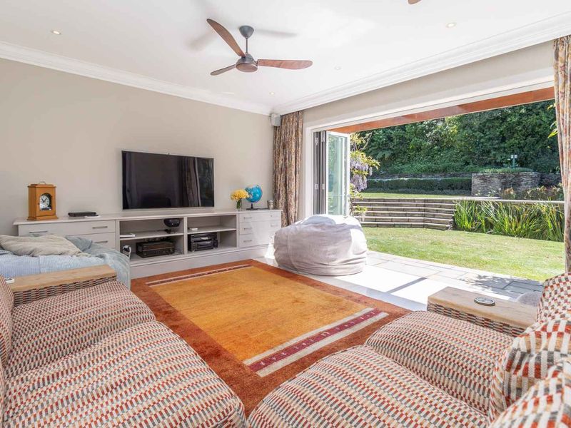 Spacious living room featuring built-in cabinetry, ceiling fan, and large bi-fold doors opening onto a landscaped garden patio.