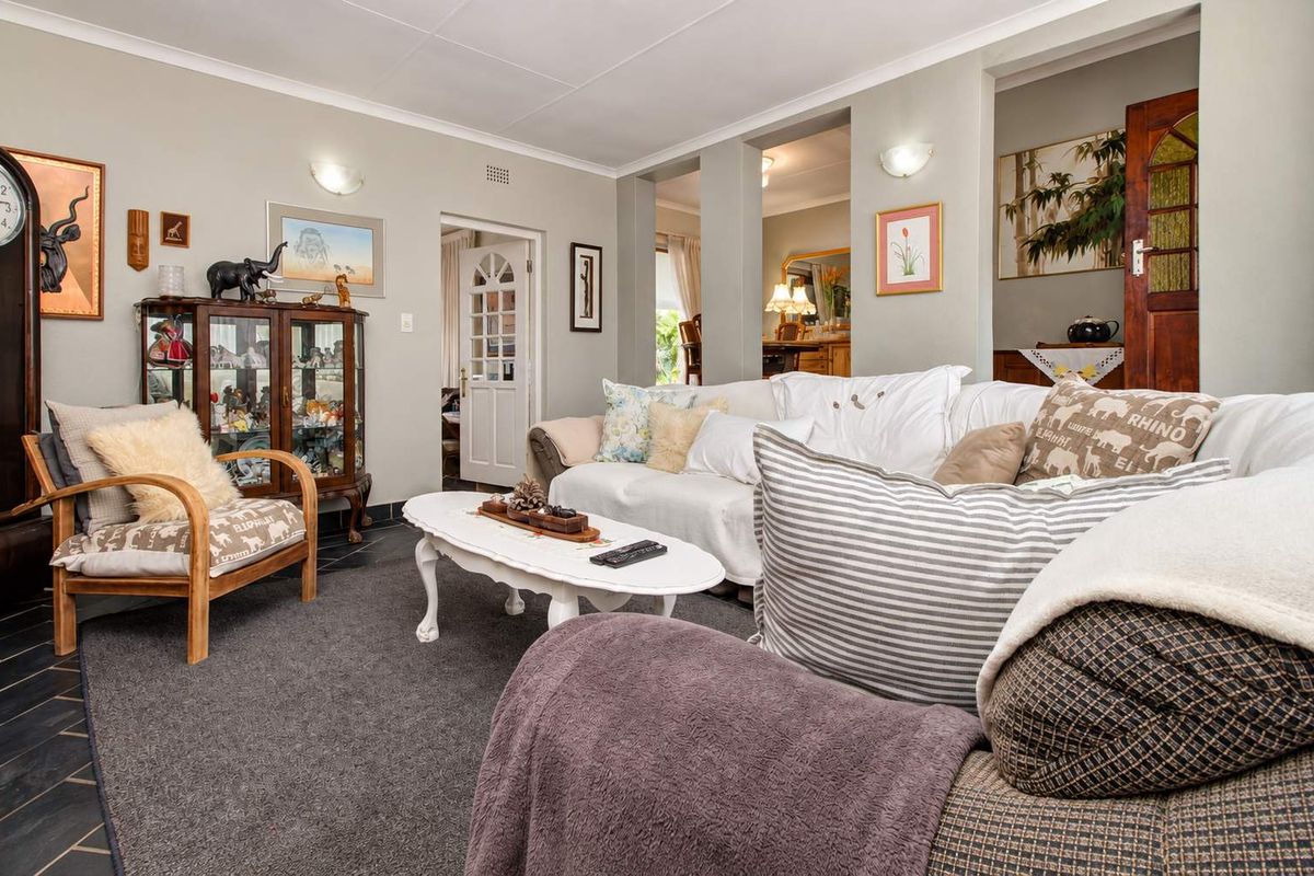 A comfortable living room featuring a mix of tiled and carpeted flooring, coved ceilings, and wall sconce lighting, with access to adjacent living spaces.
