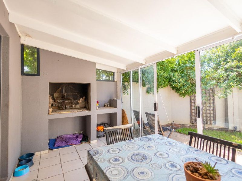 Covered patio area featuring a built-in braai, tiled flooring, and large sliding glass doors providing seamless access to the garden.