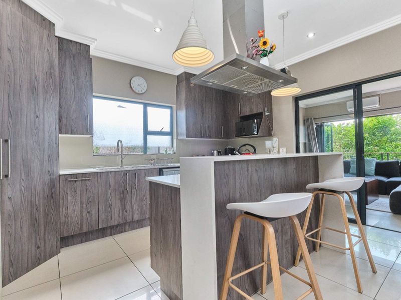 Modern kitchen featuring wood-grain cabinetry, stone countertops, stainless steel extractor fan, and seamless flow to an outdoor patio area through sliding glass doors.