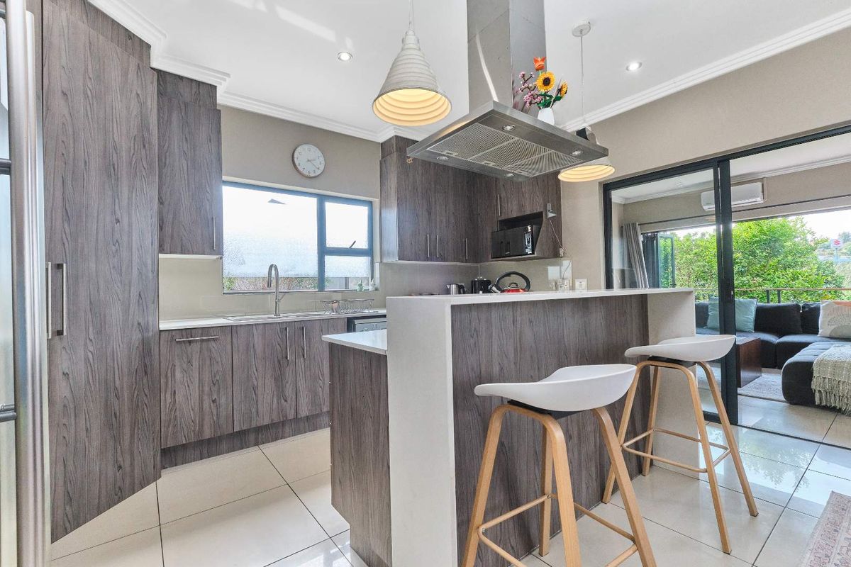 Modern kitchen featuring wood-grain cabinetry, stone countertops, stainless steel extractor fan, and seamless flow to an outdoor patio area through sliding glass doors.