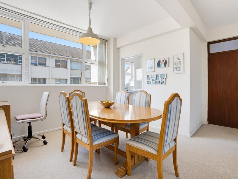 A bright dining room featuring large windows, neutral carpet flooring, and a central pendant light, offering a functional space for meals.