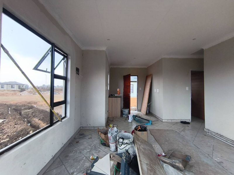 An unfinished living area featuring tiled flooring, aluminium windows, and recessed lighting, currently undergoing final construction and cleanup phases.