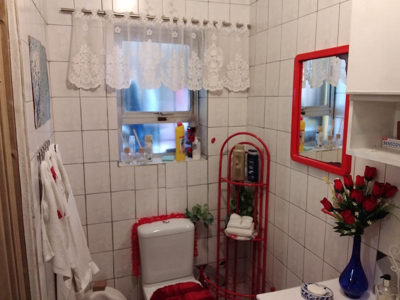 A compact bathroom featuring full-height ceramic wall tiling, a standard toilet, and a window, offering a functional space in need of cosmetic updates.