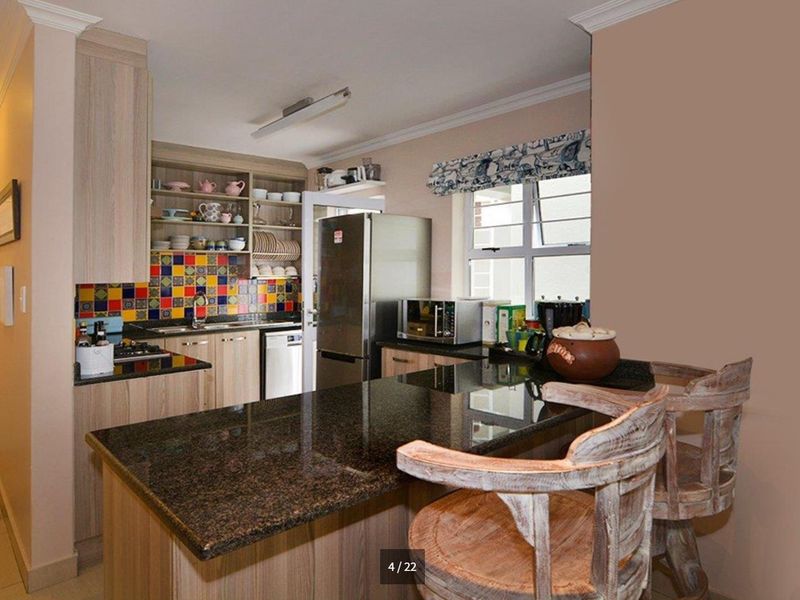 A functional kitchen featuring granite countertops, wood-finish cabinetry, and a vibrant tiled backsplash, offering a practical layout with a breakfast bar area.