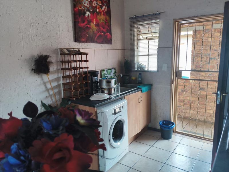A compact kitchen area featuring built-in cabinetry, a stainless steel sink, tiled flooring, and direct access to an outdoor area through a security gate.