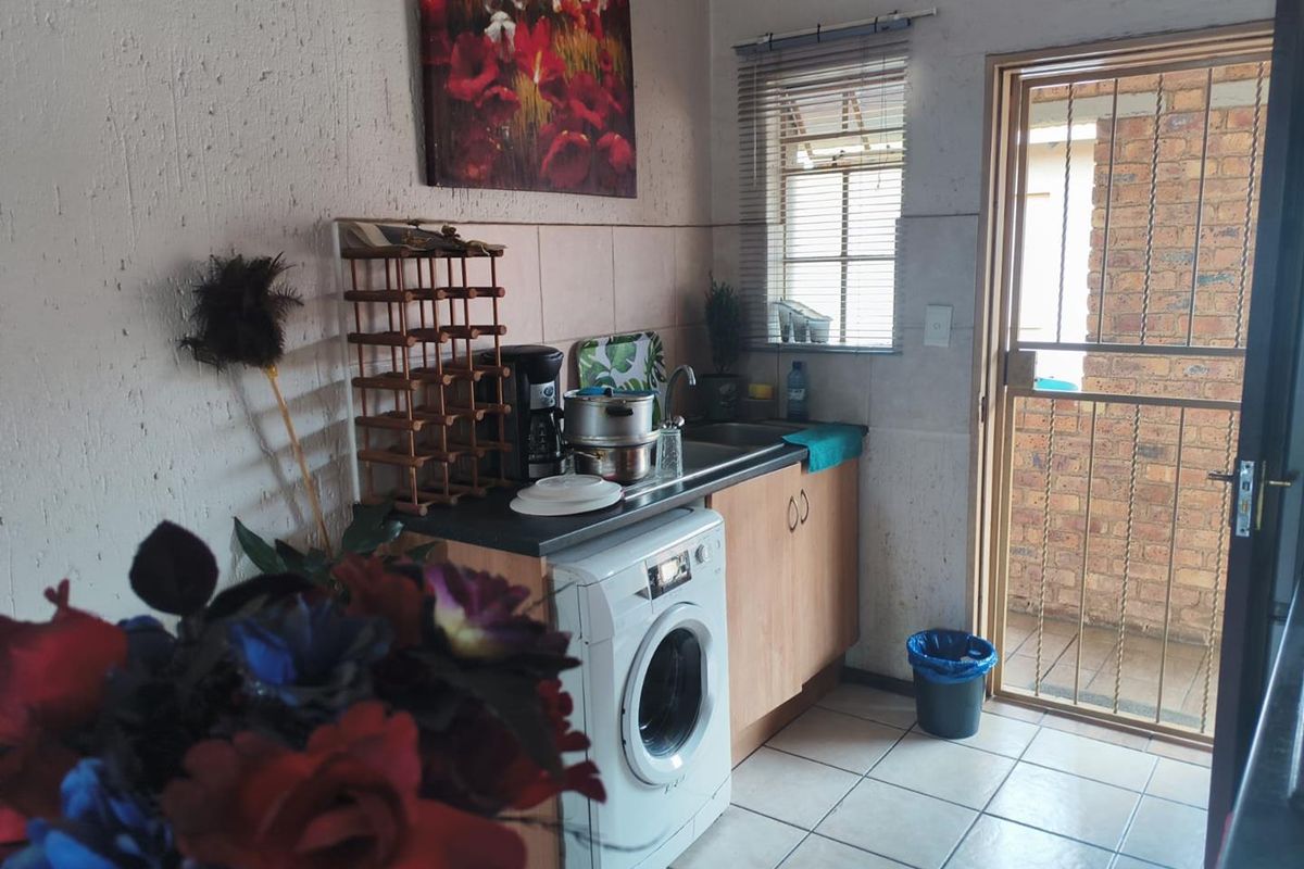 A compact kitchen area featuring built-in cabinetry, a stainless steel sink, tiled flooring, and direct access to an outdoor area through a security gate.