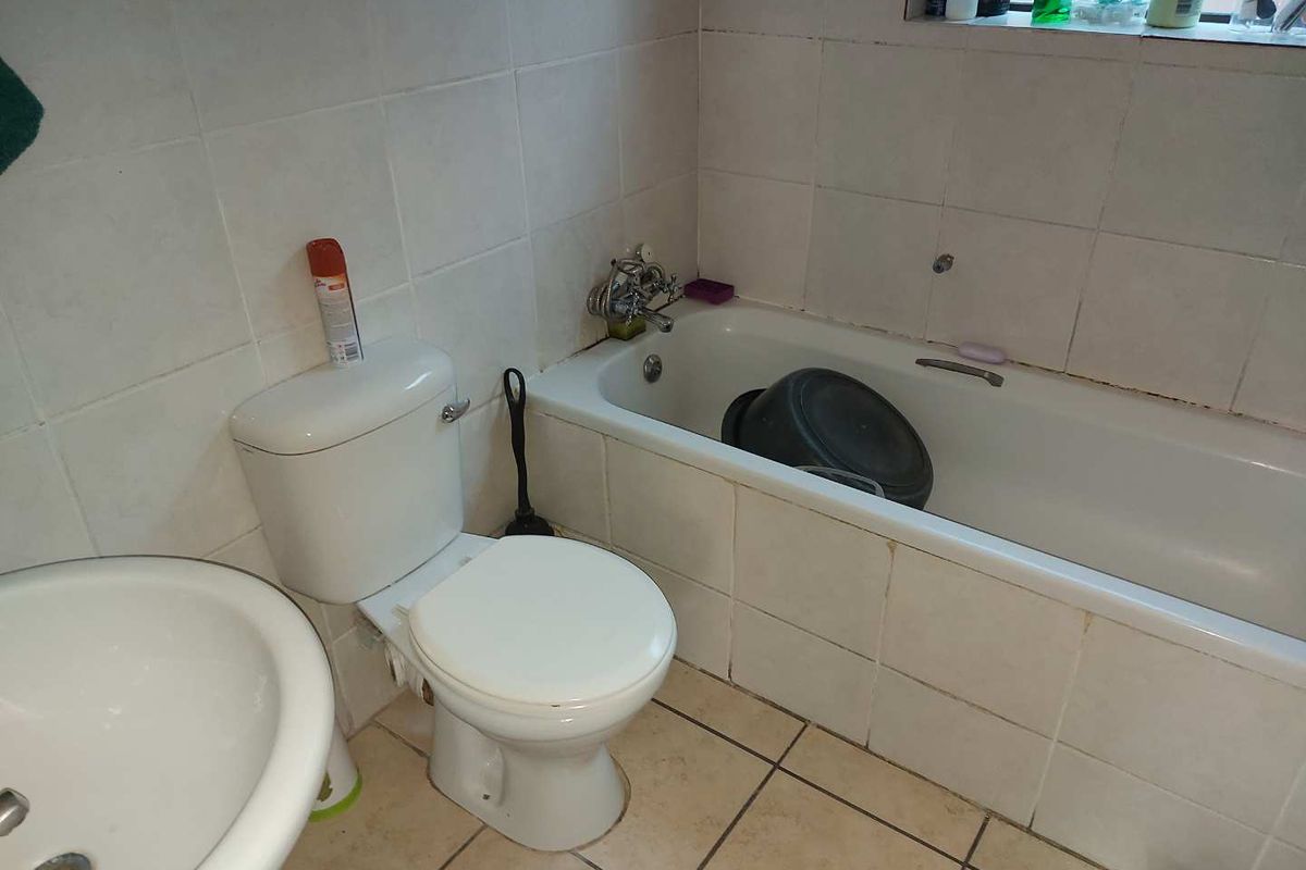 A functional bathroom featuring a standard bathtub, pedestal basin, and toilet with tiled walls and flooring, requiring cosmetic updates to grout and sealant.