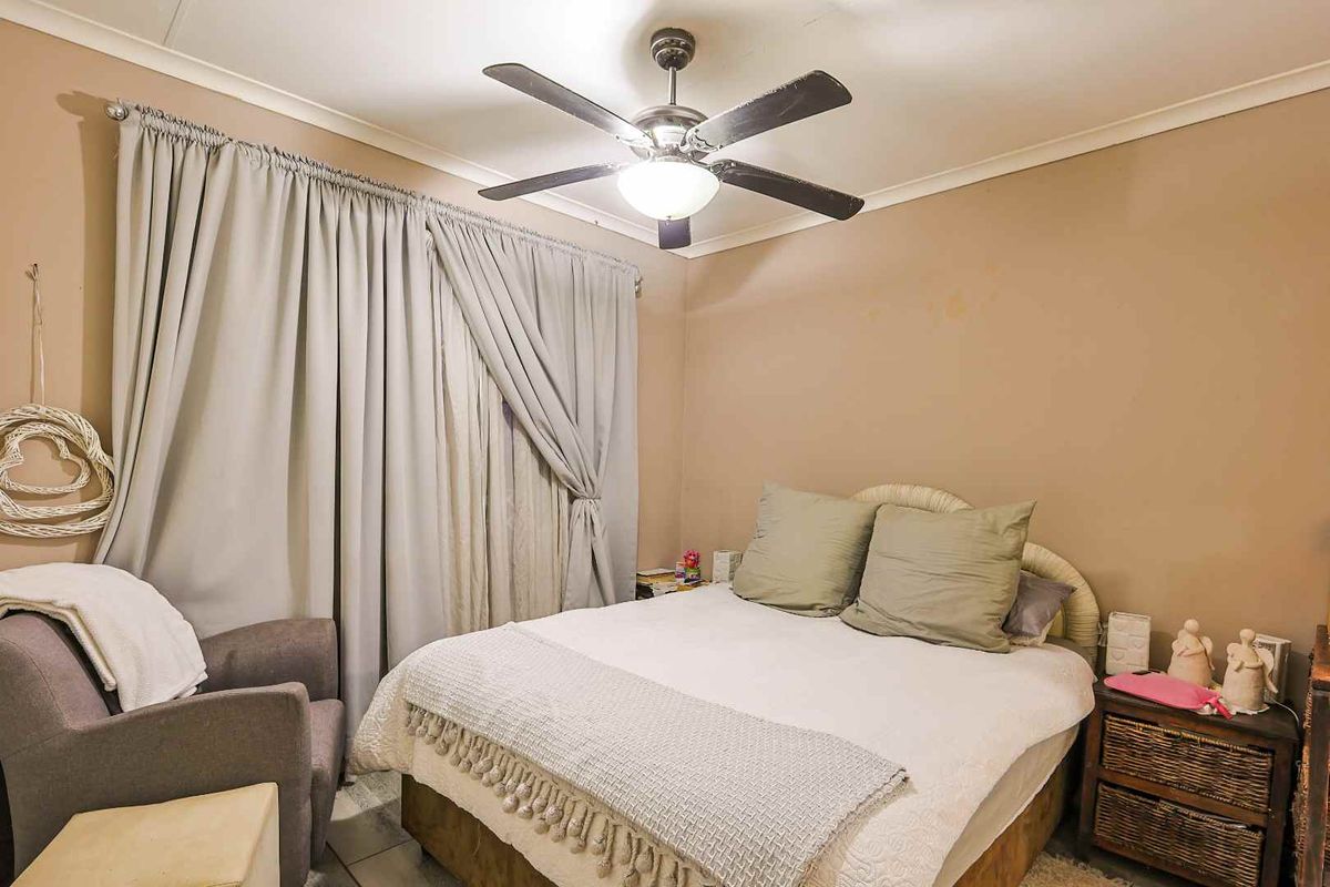 A bedroom featuring tiled flooring, a central ceiling fan, and neutral wall tones, offering a functional space ready for cosmetic updates.