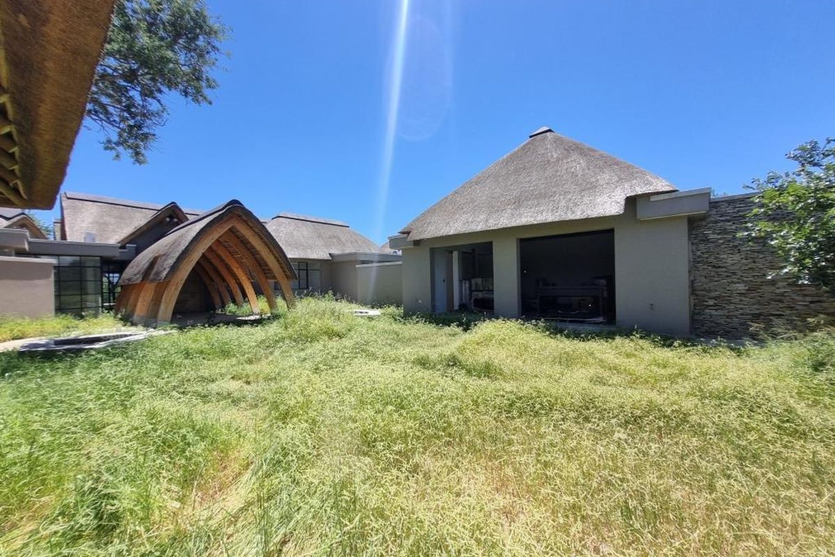Exterior view of a property featuring multiple structures with traditional thatch roofing and stone cladding, set within an expansive, overgrown garden area.