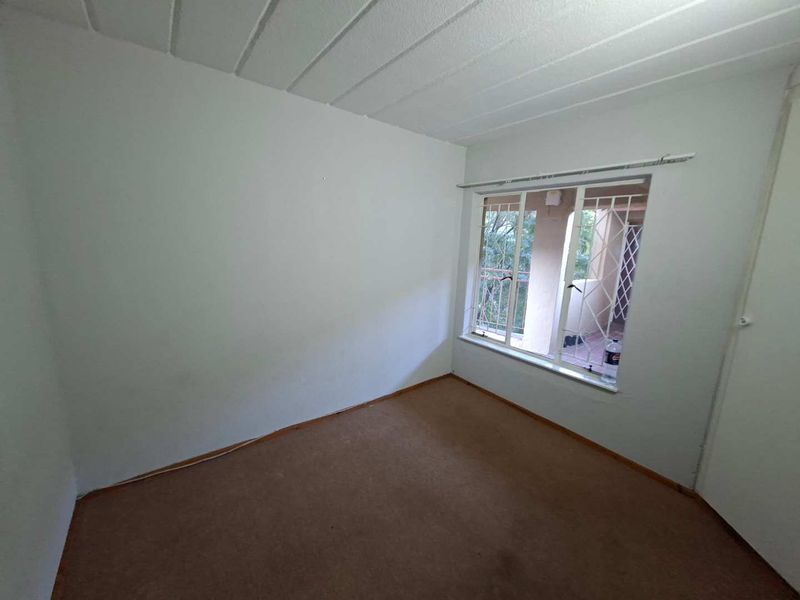 An empty bedroom featuring carpeted flooring, a textured ceiling, and a window fitted with security bars, offering a blank canvas for renovation.