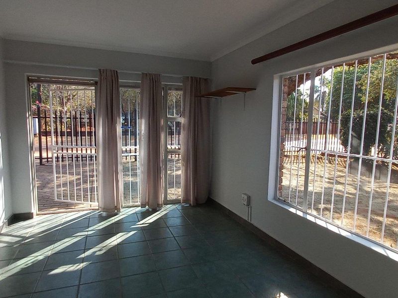 A bright, empty living room featuring tiled flooring, large windows with security bars, and a sliding glass door leading to the exterior.