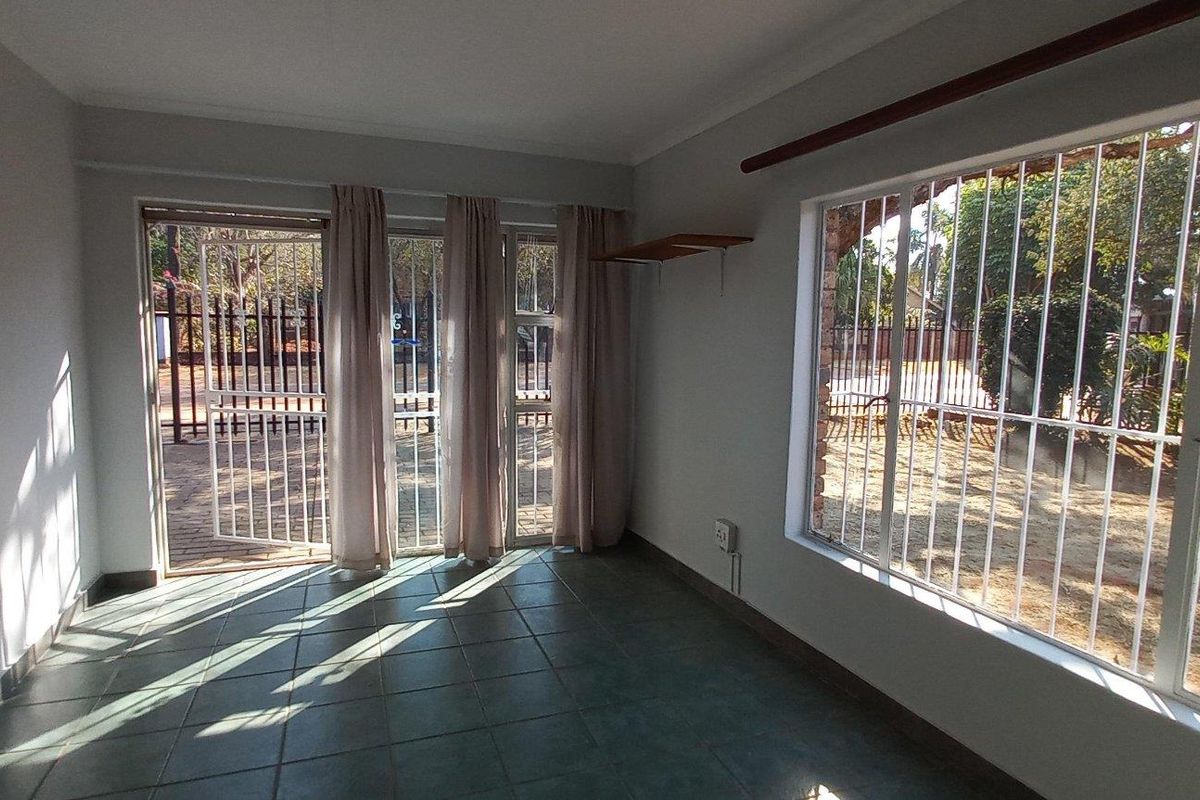 A bright, empty living room featuring tiled flooring, large windows with security bars, and a sliding glass door leading to the exterior.