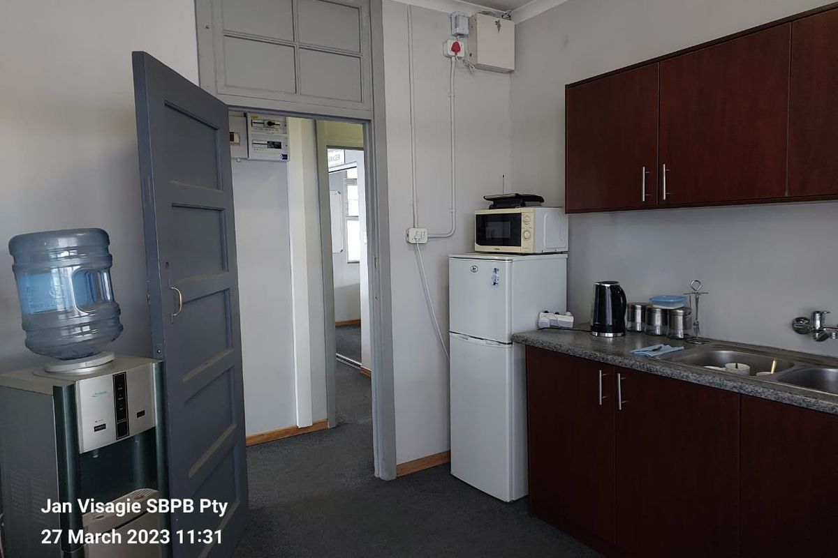 A functional kitchenette area featuring dark wood cabinetry, a stainless steel sink, and direct access to an adjacent office space.