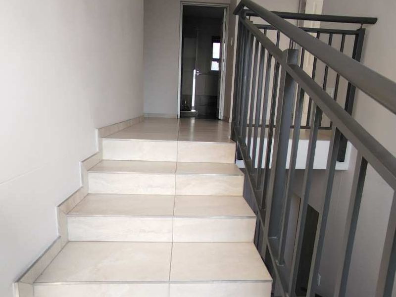 A clean, modern staircase featuring light-toned floor tiles and a sturdy metal balustrade, leading to an upper-level landing.