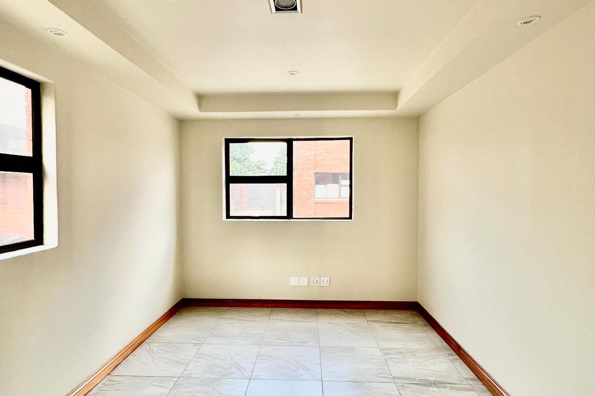A bright, empty bedroom featuring neutral walls, tiled flooring, recessed ceiling lighting, and dark-framed windows.