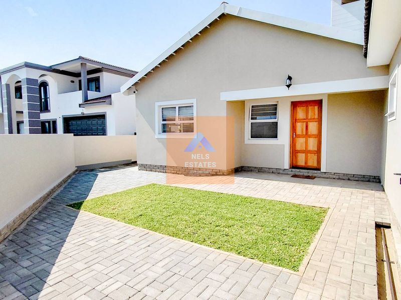 A well-maintained front exterior featuring a paved driveway, a small lawn area, and a solid timber entrance door.