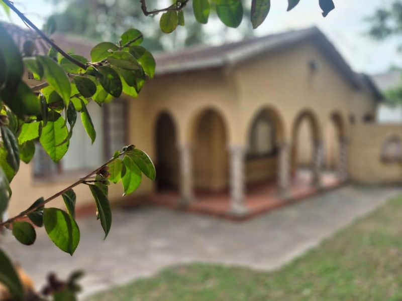 Front view of a house featuring a covered veranda with arched openings and decorative columns, set back from a concrete driveway.