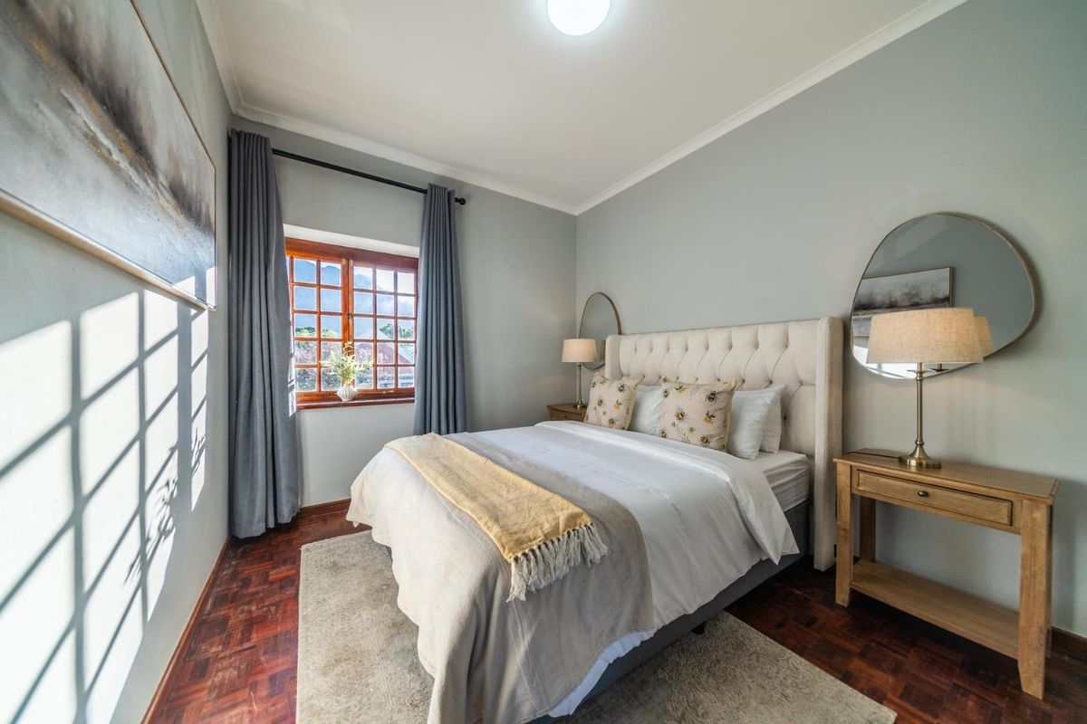 A well-maintained bedroom featuring warm parquet flooring, a classic timber-framed window, and neutral wall finishes.