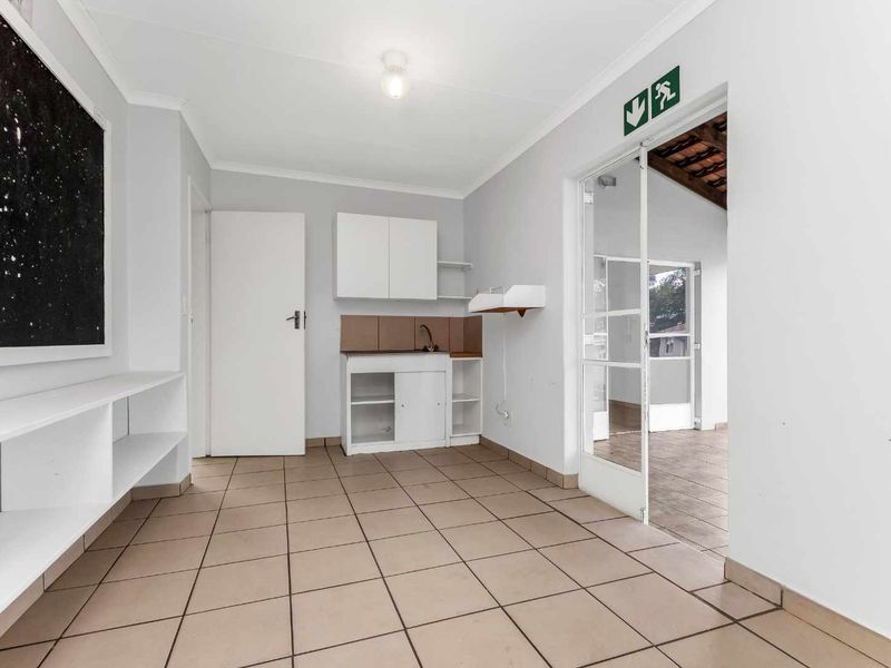 A functional scullery or utility area featuring tiled flooring, built-in cabinetry with a sink, and direct access to an adjacent patio space.