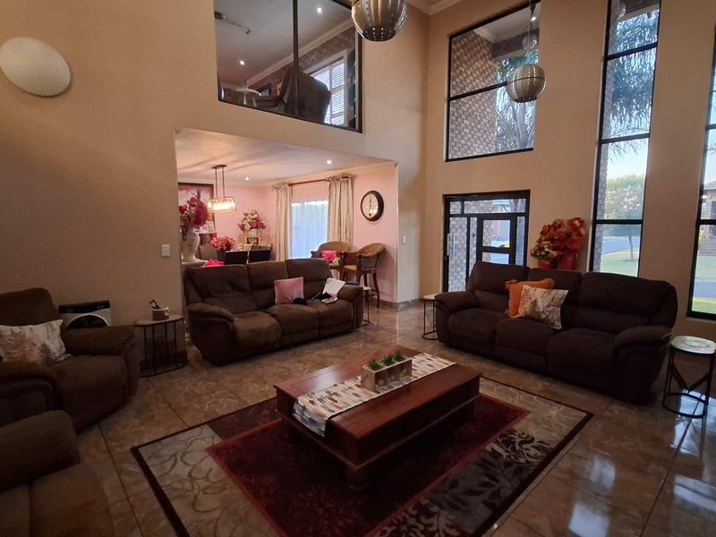 Spacious open-plan living area featuring double-volume ceilings, large windows providing ample natural light, and tiled flooring with a mezzanine level overlooking the space.