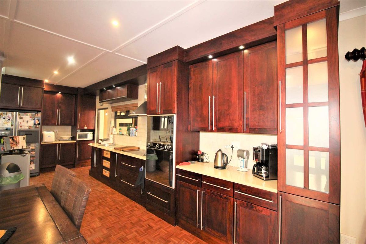 A spacious kitchen featuring dark wood cabinetry, integrated oven, stainless steel extractor fan, and ample counter space with recessed lighting.