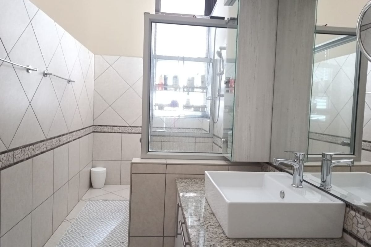 A modern bathroom featuring a granite vanity top, vessel sink, tiled walls with decorative border, and a glass-enclosed shower area.