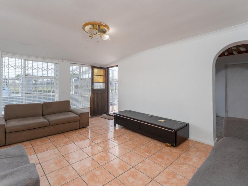 A living room featuring tiled flooring, an arched entryway, and security gates on the windows and door.