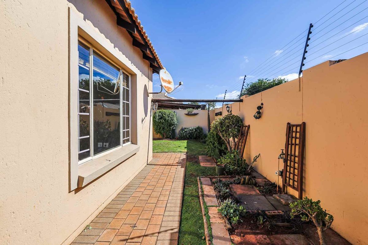 A side garden pathway featuring paved walkways, established garden beds, and perimeter walling with integrated electric fencing.