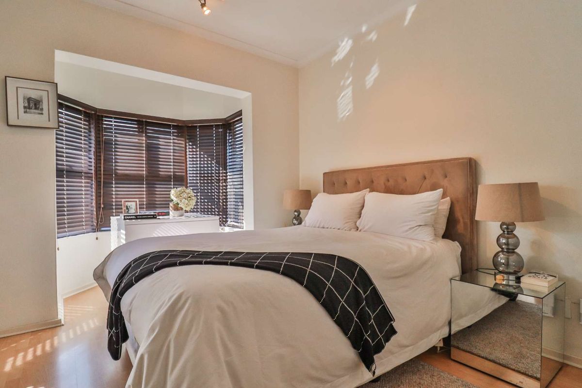A well-lit bedroom featuring a bay window with fitted wooden blinds and neutral wall finishes.