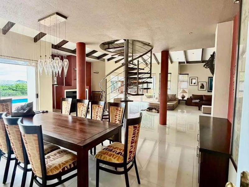 Spacious open-plan living and dining area featuring a striking spiral staircase, exposed ceiling beams, and large sliding doors leading to the outdoor pool area.