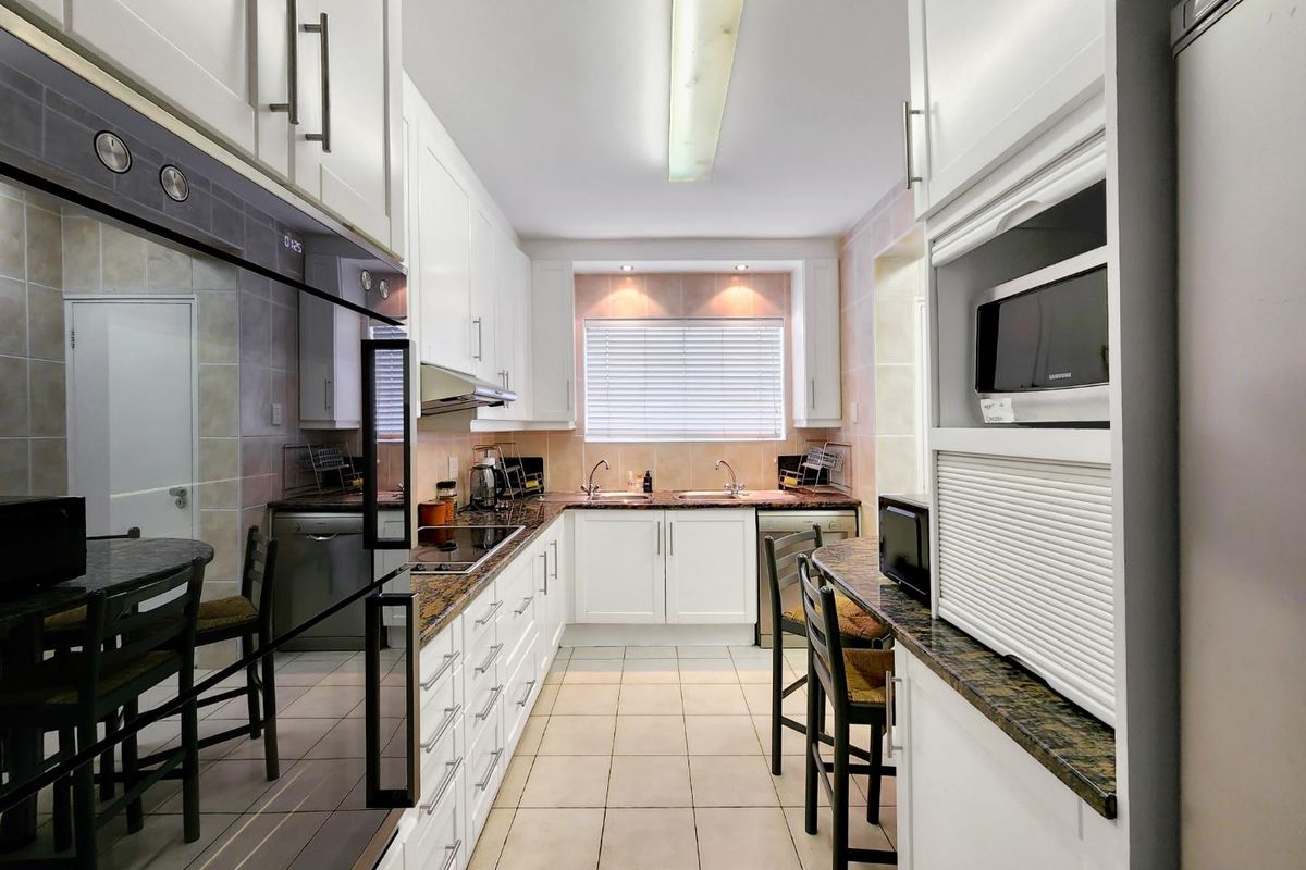 A well-maintained galley-style kitchen featuring white cabinetry, granite countertops, integrated appliances, and tiled flooring with ample storage space.
