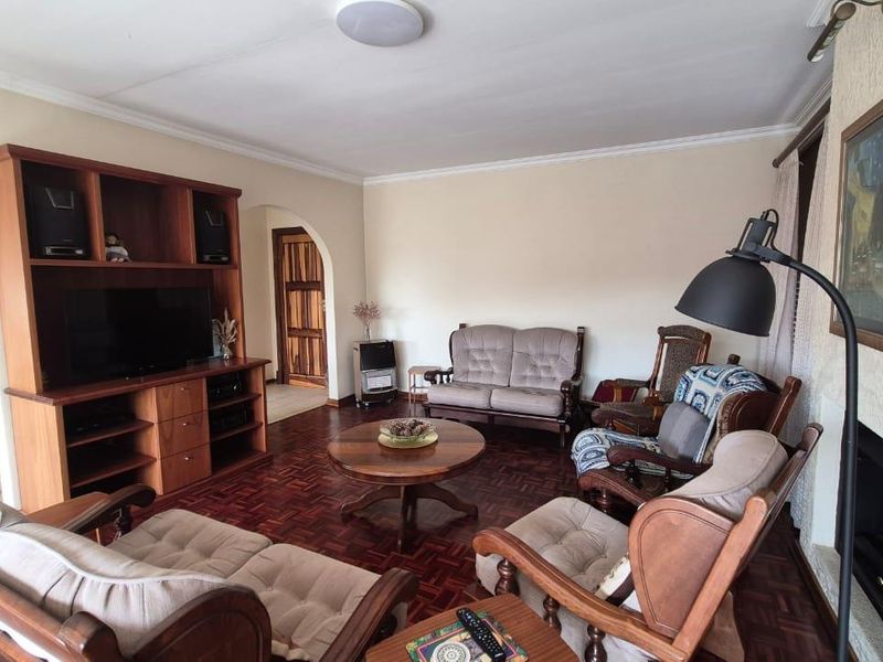 A living room featuring classic parquet flooring, a built-in wooden shelving unit, and a fireplace, connected to other areas via an archway.
