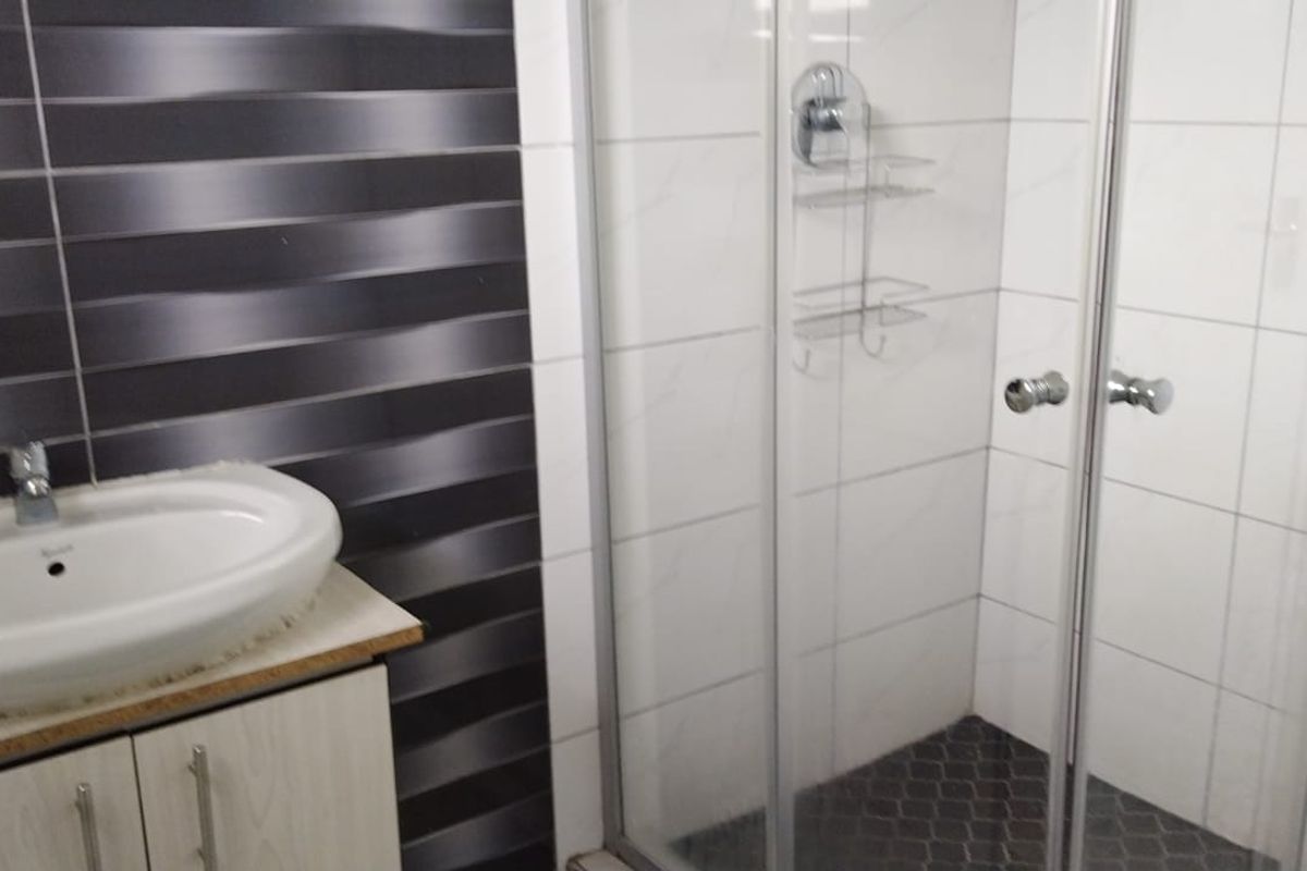 A modern bathroom featuring a vanity cabinet with a ceramic basin and a glass-enclosed shower with tiled walls.