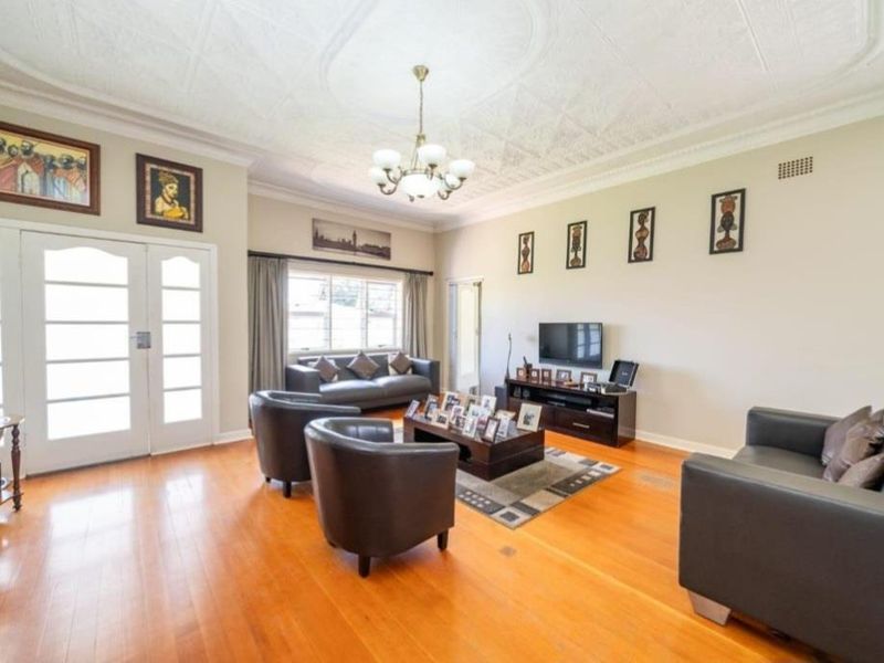 Spacious living room featuring polished hardwood flooring, an ornate plaster ceiling, and classic french doors providing natural light.