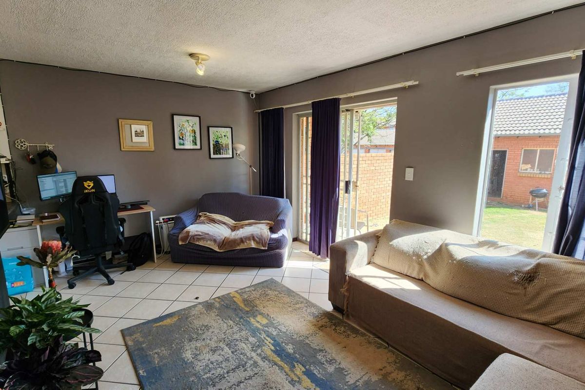 A living room featuring tiled flooring, large windows, and a sliding glass door providing access to the rear garden area.