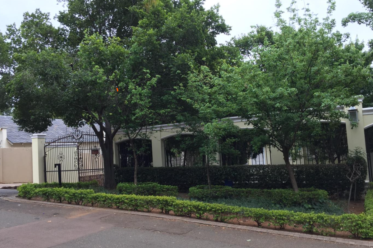 Front view of the property featuring a secure wrought iron gate, established perimeter wall, and mature landscaped garden.