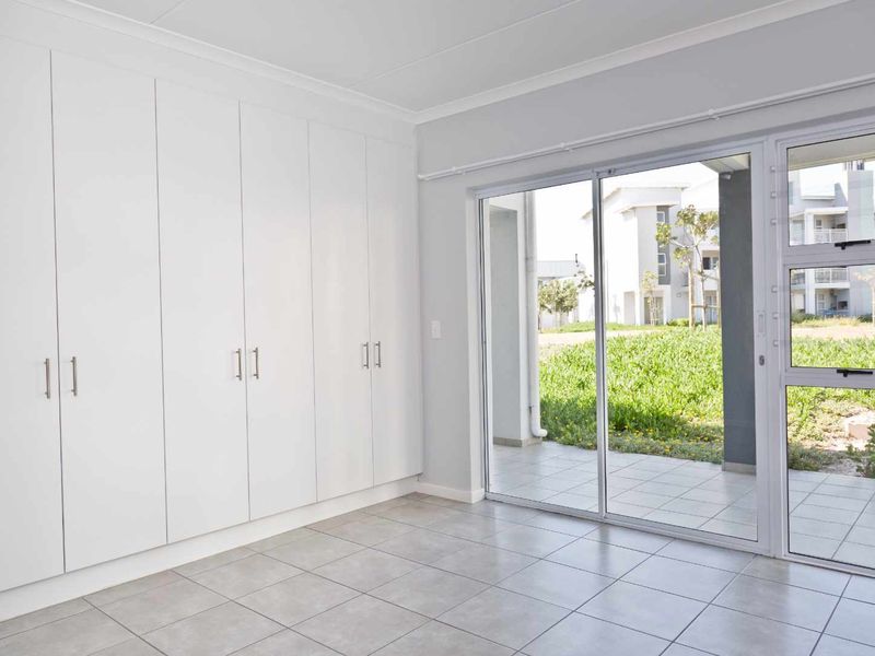 A bright, empty bedroom featuring extensive built-in cupboards, tiled flooring, and a sliding glass door providing direct access to an outdoor patio area.