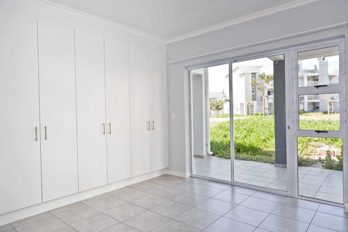 A bright, empty bedroom featuring extensive built-in cupboards, tiled flooring, and a sliding glass door providing direct access to an outdoor patio area.