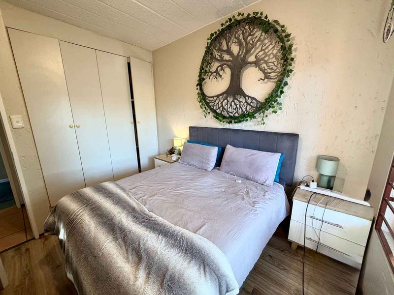 A bedroom featuring laminate flooring and a built-in wardrobe, with walls showing signs of wear and texture.