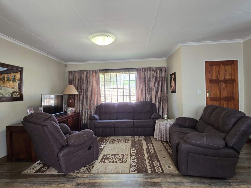 A comfortable living room featuring laminate flooring, coved ceilings, and a window with security bars, providing a functional and well-maintained space.
