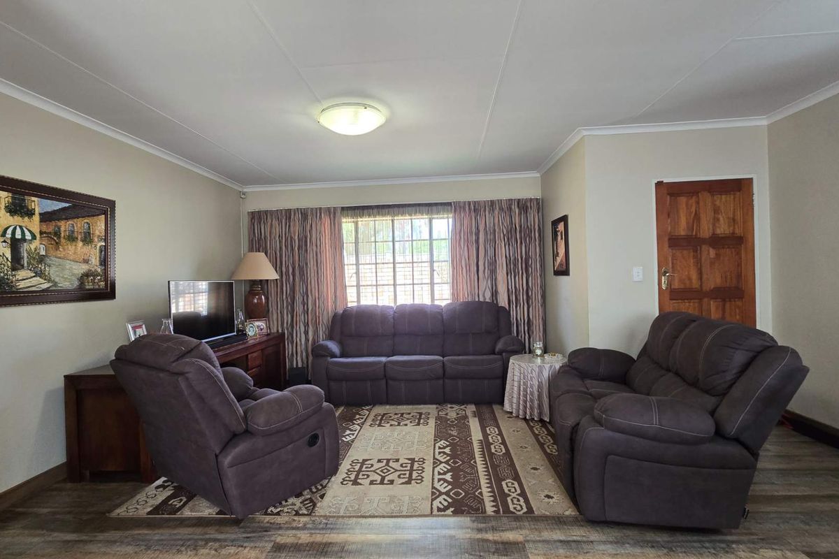A comfortable living room featuring laminate flooring, coved ceilings, and a window with security bars, providing a functional and well-maintained space.