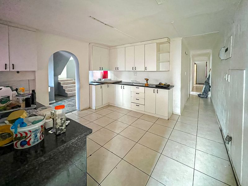A functional kitchen featuring white built-in cabinetry, dark countertops, and tiled flooring, connected to a hallway and an arched entryway.