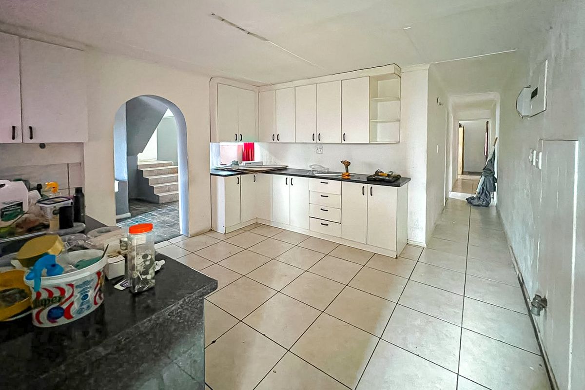 A functional kitchen featuring white built-in cabinetry, dark countertops, and tiled flooring, connected to a hallway and an arched entryway.